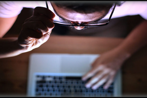 a man peers over his glasses at information on a computer screen