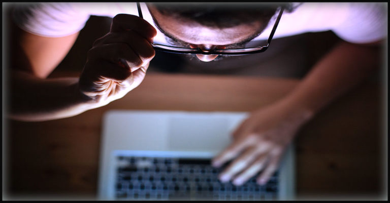 a man peers over his glasses at information on a computer screen