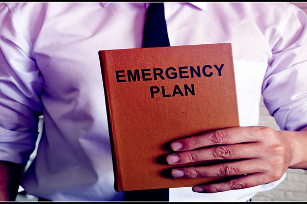 a brown notebook entitled "Emergency Plan" is held by a white man in business attire