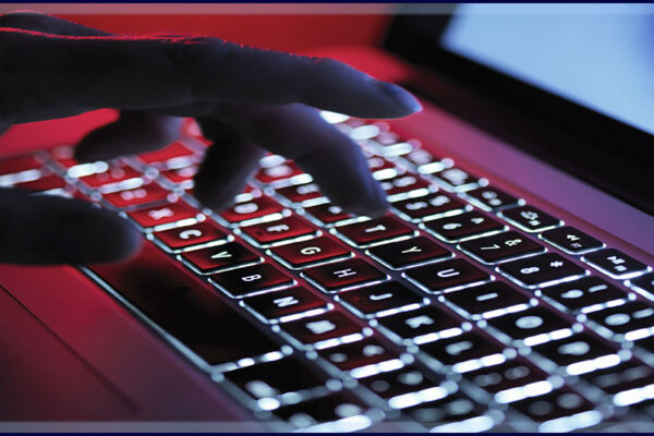 a shadowy caucasioan hand types on a backlit laptop in a dim room