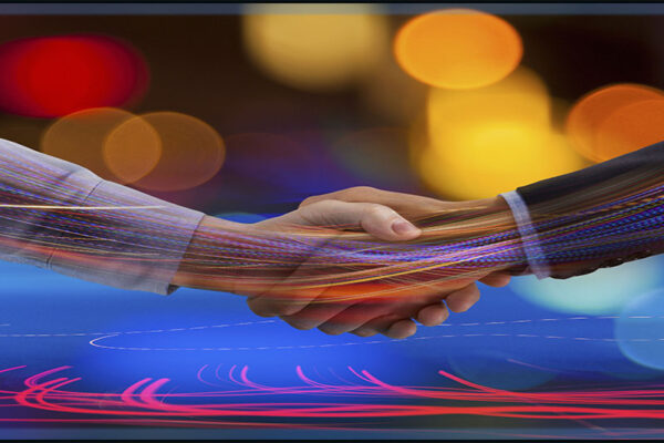 two caucasian business professional handa are depicted shaking on a business deal over a blurred background of tech cconnection imagery